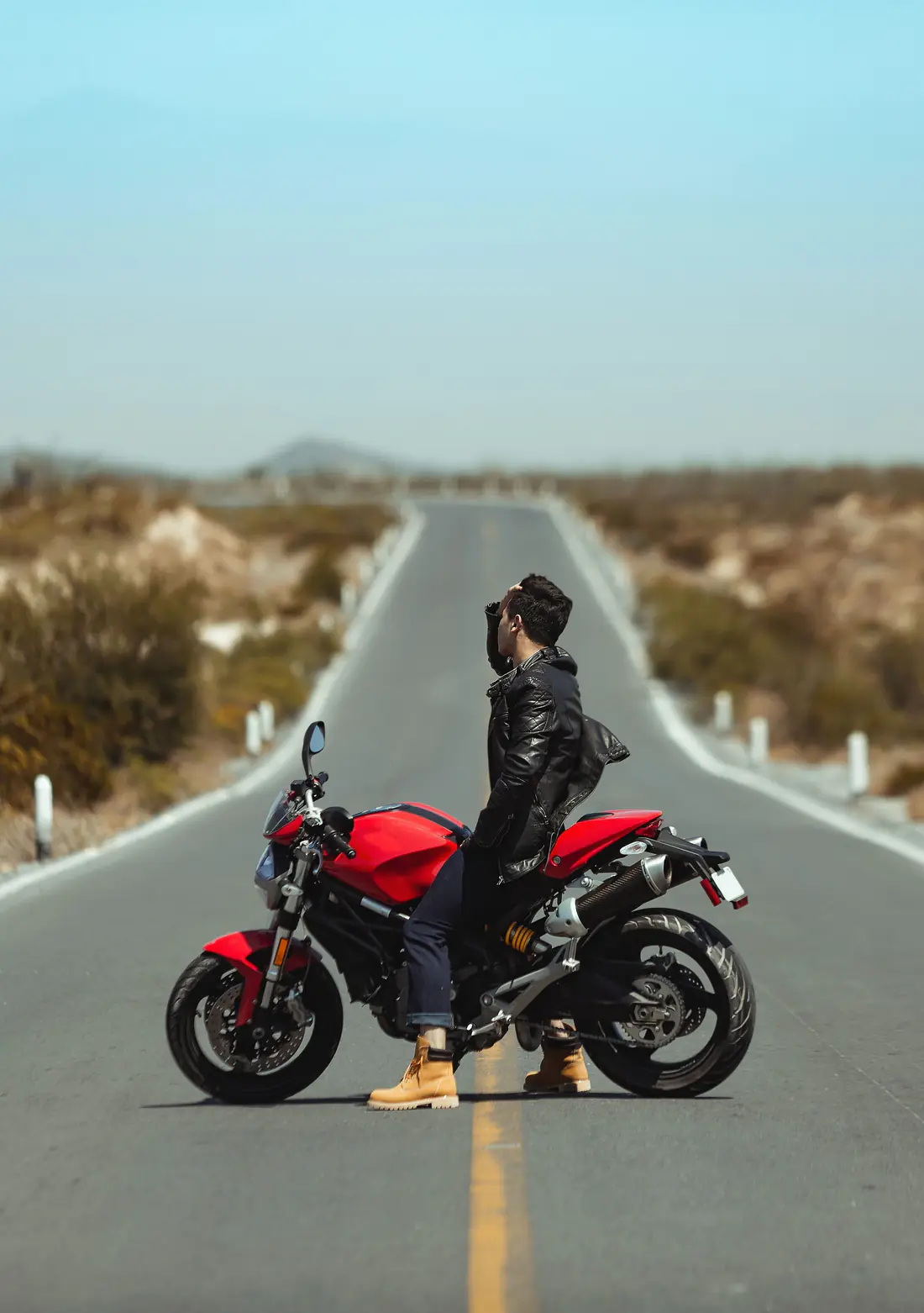 Illustrative stock photograph of a rider standing beside a red motorcycle on a wide road