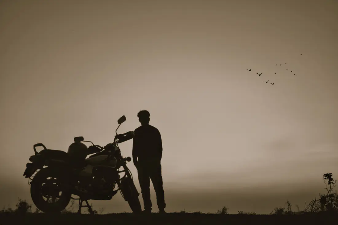 Illustrative stock photograph of a person standing beside a motorcycle at sunset